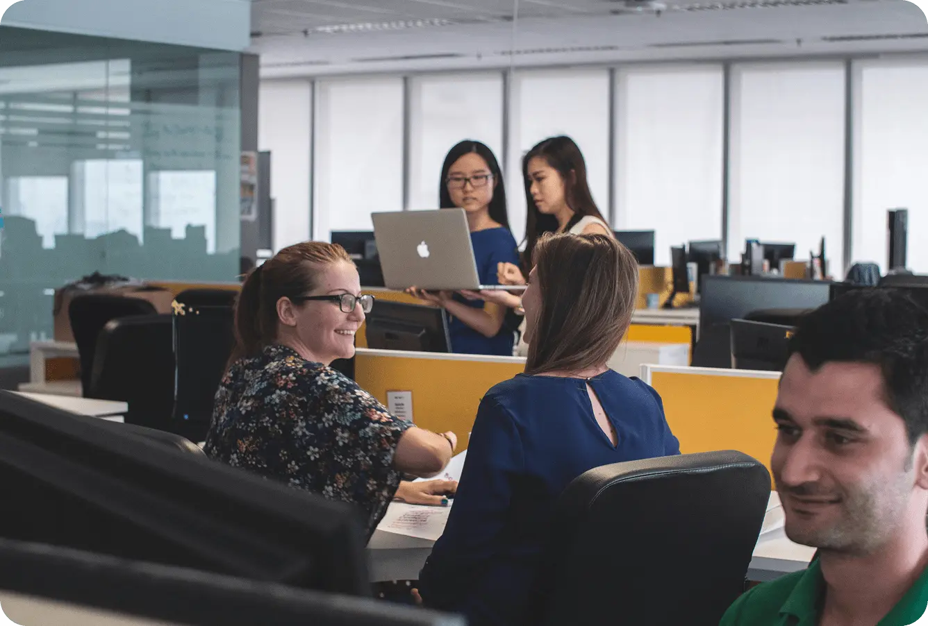 A lively office scene with five colleagues engaged in discussions and teamwork