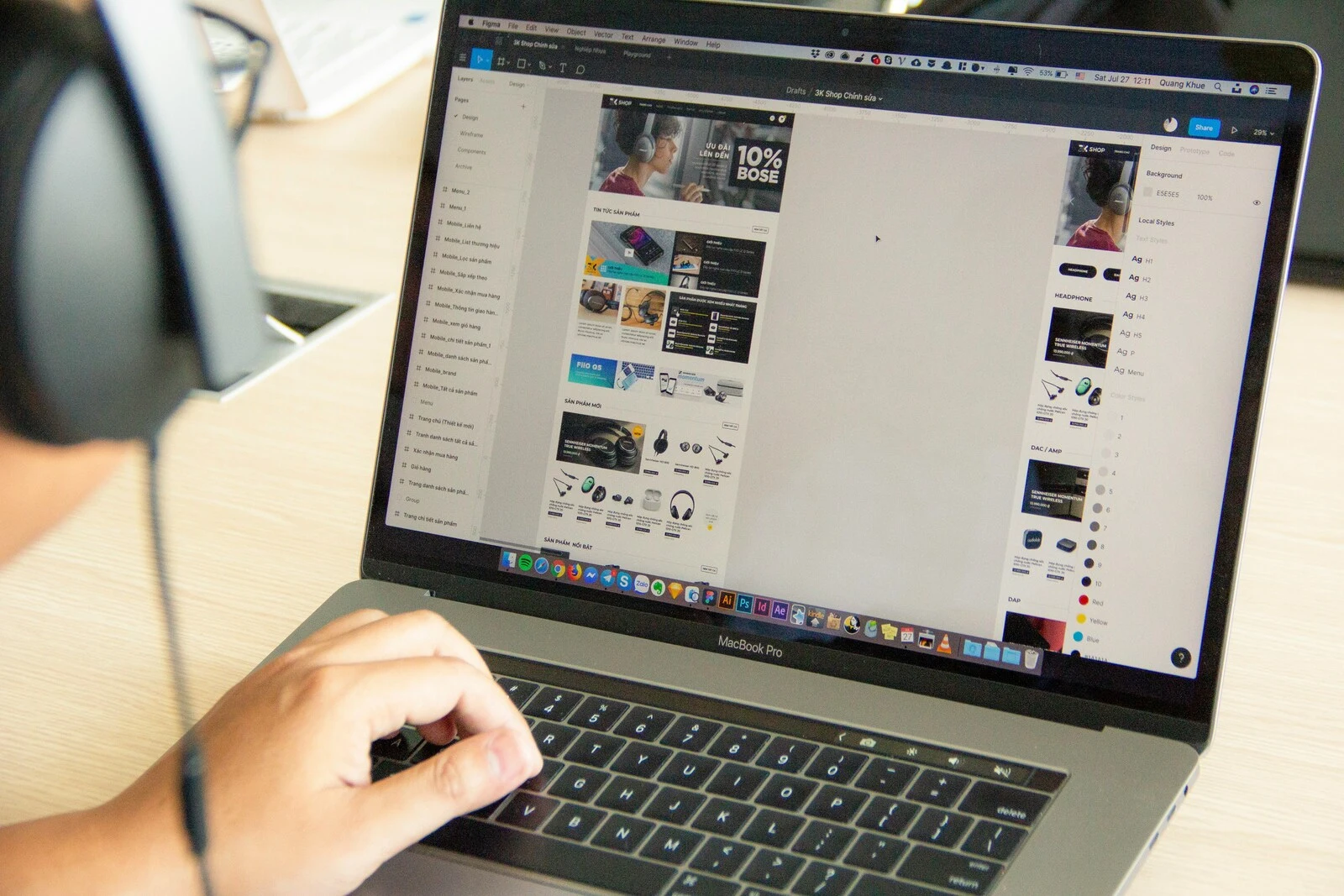 A person wearing headphones works on a laptop displaying a design project. The screen shows a layout with images and text, conveying focus and creativity