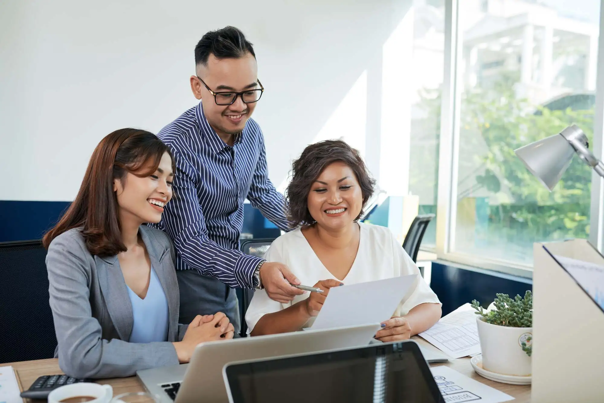 Three colleagues in a bright office, smiling while discussing a document