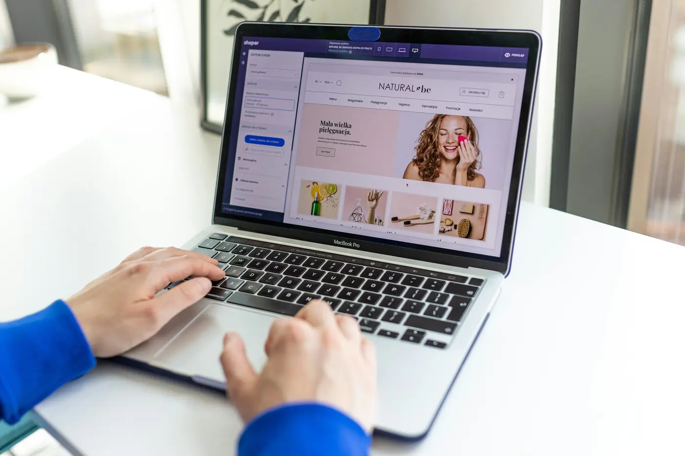 Hands typing on a laptop displaying a bright beauty and lifestyle webpage with a smiling woman, product photos, and navigation menu