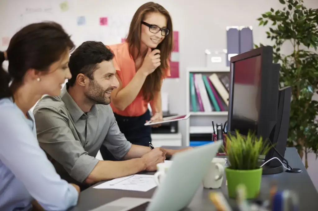 Three coworkers gather around a desktop computer in a bright office, sharing ideas with focused, collaborative expressions| SEO for small business in Nepal