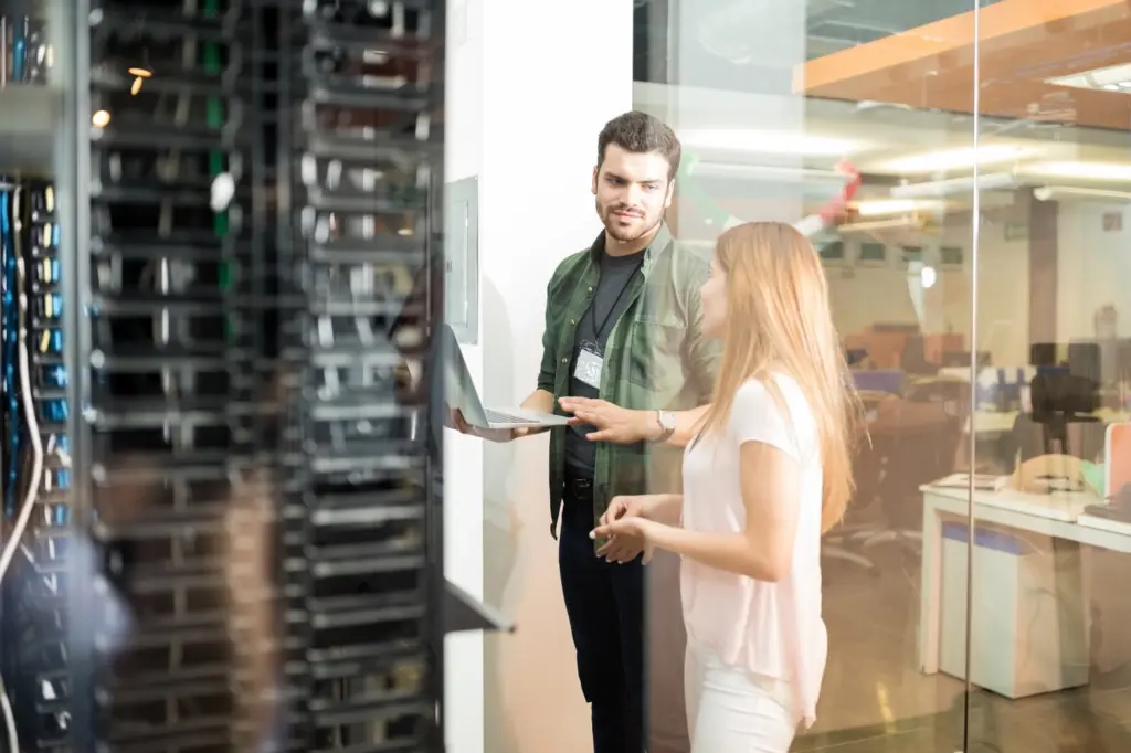 two-business-people-standing-server-room-with-laptop-discussing